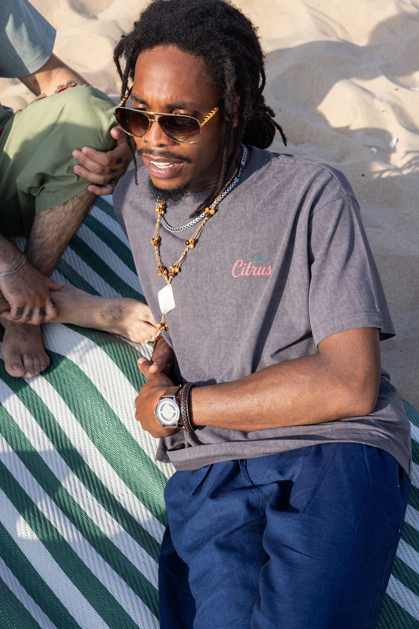 Man wearing sunglasses and a gray t-shirt with 'Citrus' logo on a sandy background