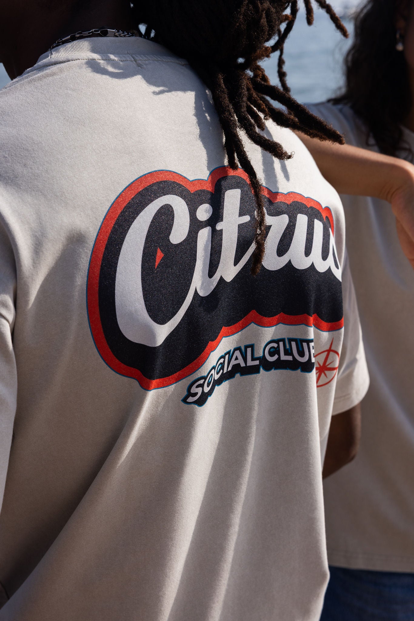 Person wearing a beige shirt with 'Citrus Social Club' logo on the back, reminiscent of 1990's skateboard fashion, bold high quality print.